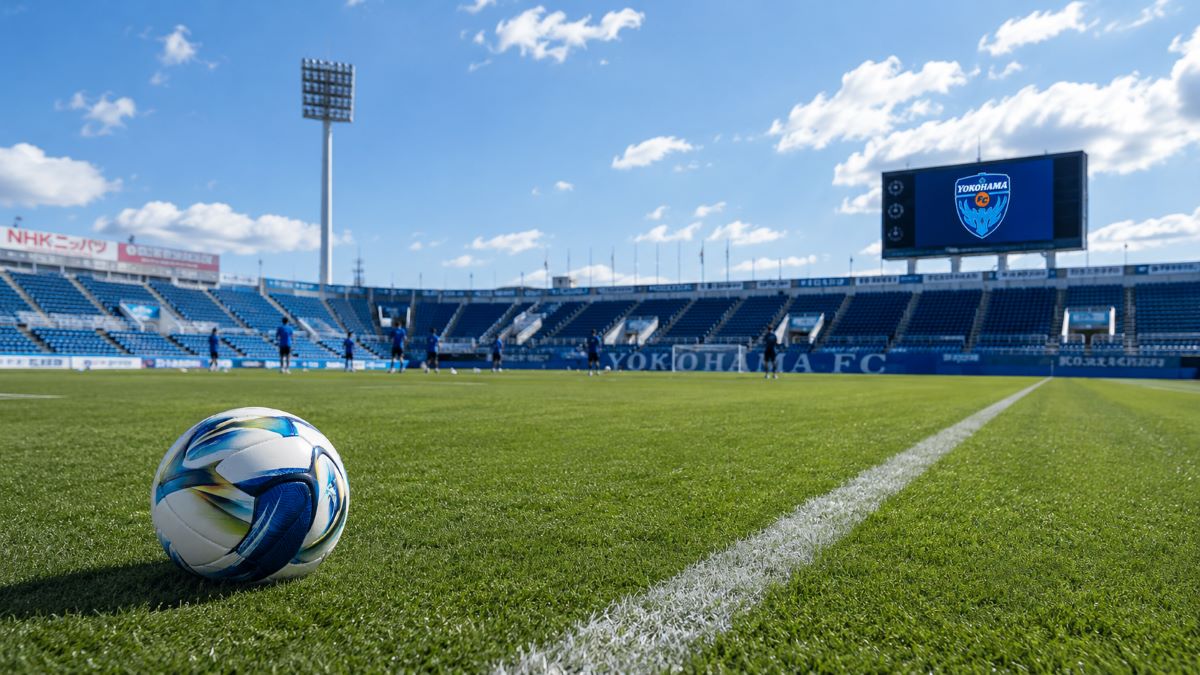 白線が奥へ伸びる日中のスタジアムで、公式球が置かれた横浜FCの試合前の風景